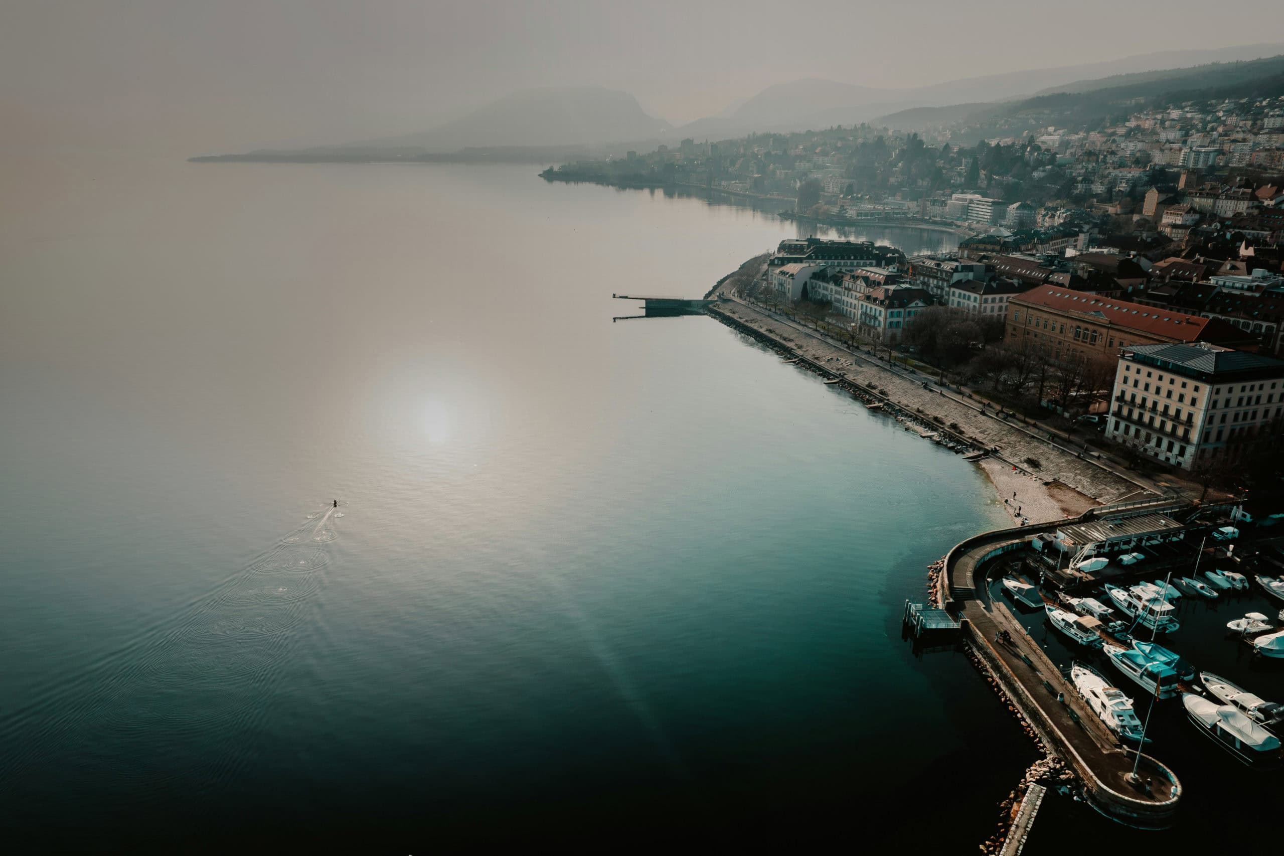 Bateaux au port de Neuchâtel avec vue sur le lac et la ville environnante, paysage paisible et touristique, idéal pour assurance navigation et loisirs nautiques.